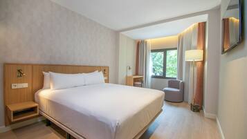 Ett hotellrum med en stor säng, sängbord, ett skrivbord, en stol och ett fönster med gardiner.
