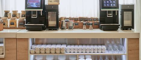 A coffee shop counter with two coffee machines, a variety of coffee beans, and neatly arranged cups and plates.