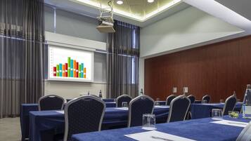 A conference room with a presentation screen displaying colorful bar graphs, a row of tables with blue tablecloths, and chairs with a star pattern.