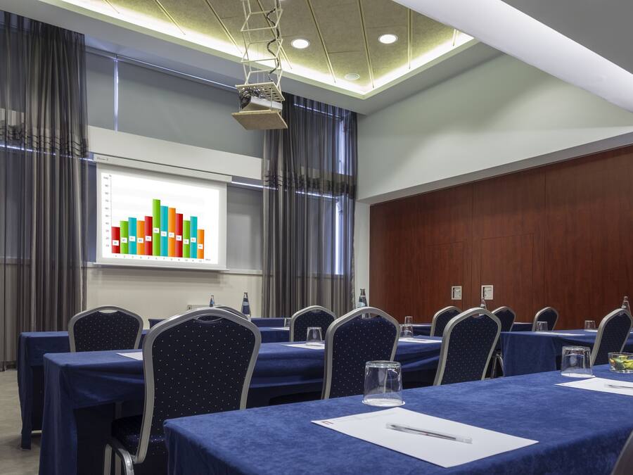A conference room with a presentation screen displaying colorful bar graphs, a row of tables with blue tablecloths, and chairs with a star pattern.