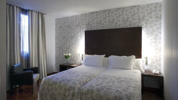 Una cama doble con ropa de cama de estampado floral, una mesita de noche con un teléfono y una silla.