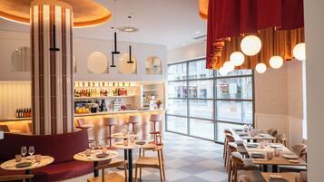 A modern restaurant interior with a bar area, seating arrangements, and large windows providing a view of the street.