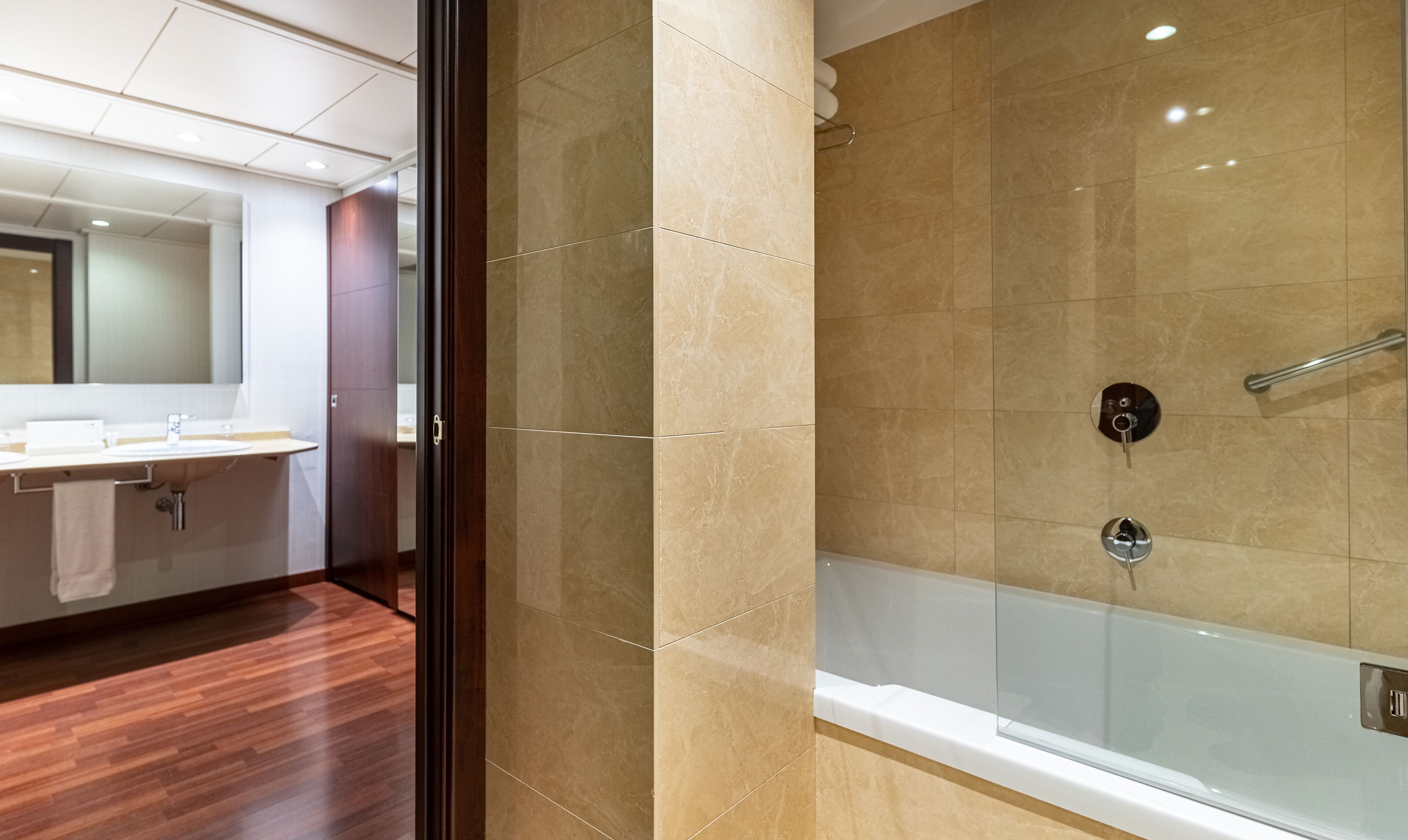 Un baño moderno con ducha de vidrio, suelo de madera y un espejo grande sobre el lavamanos.