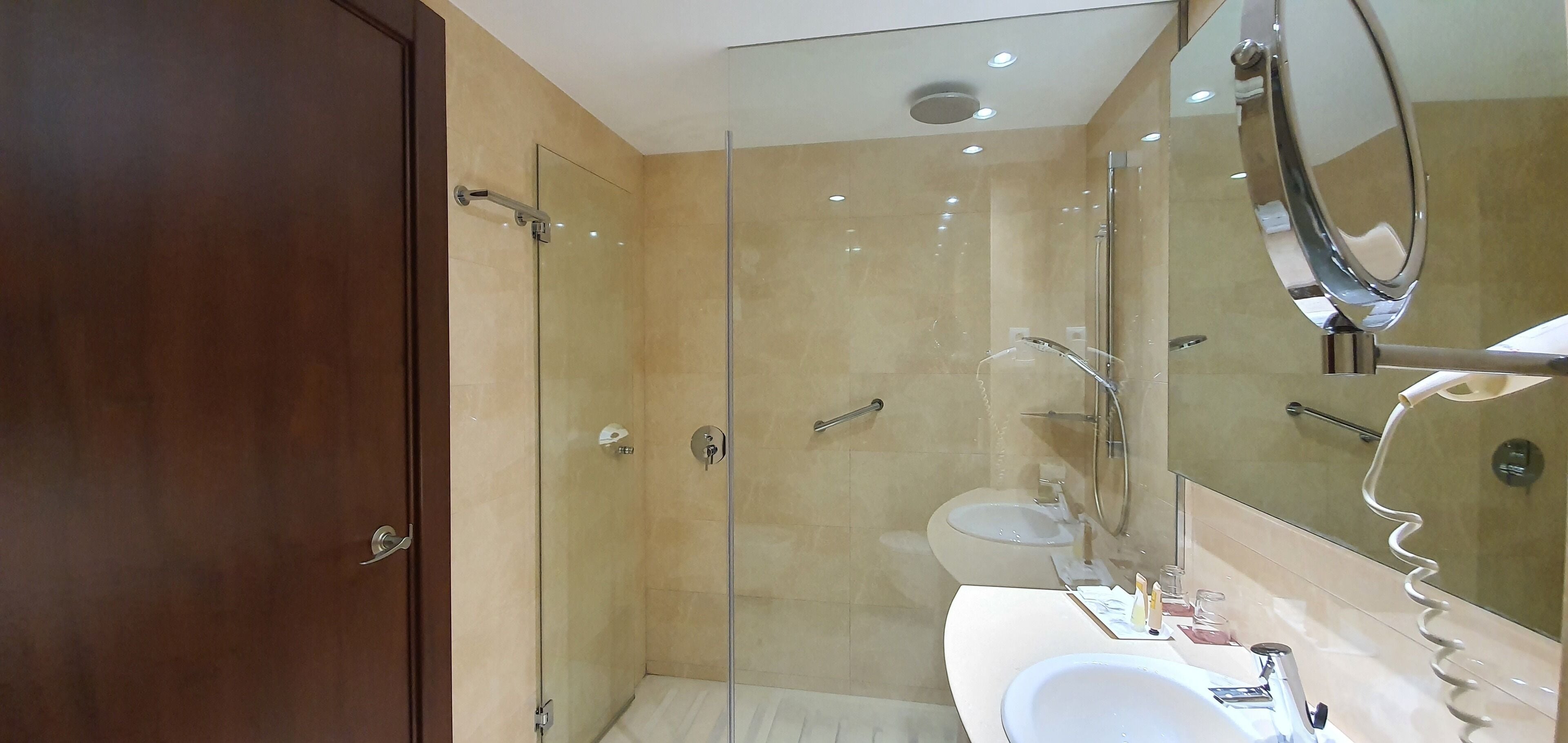 Un baño moderno con ducha envuelta en vidrio, un lavabo blanco y un espejo grande.