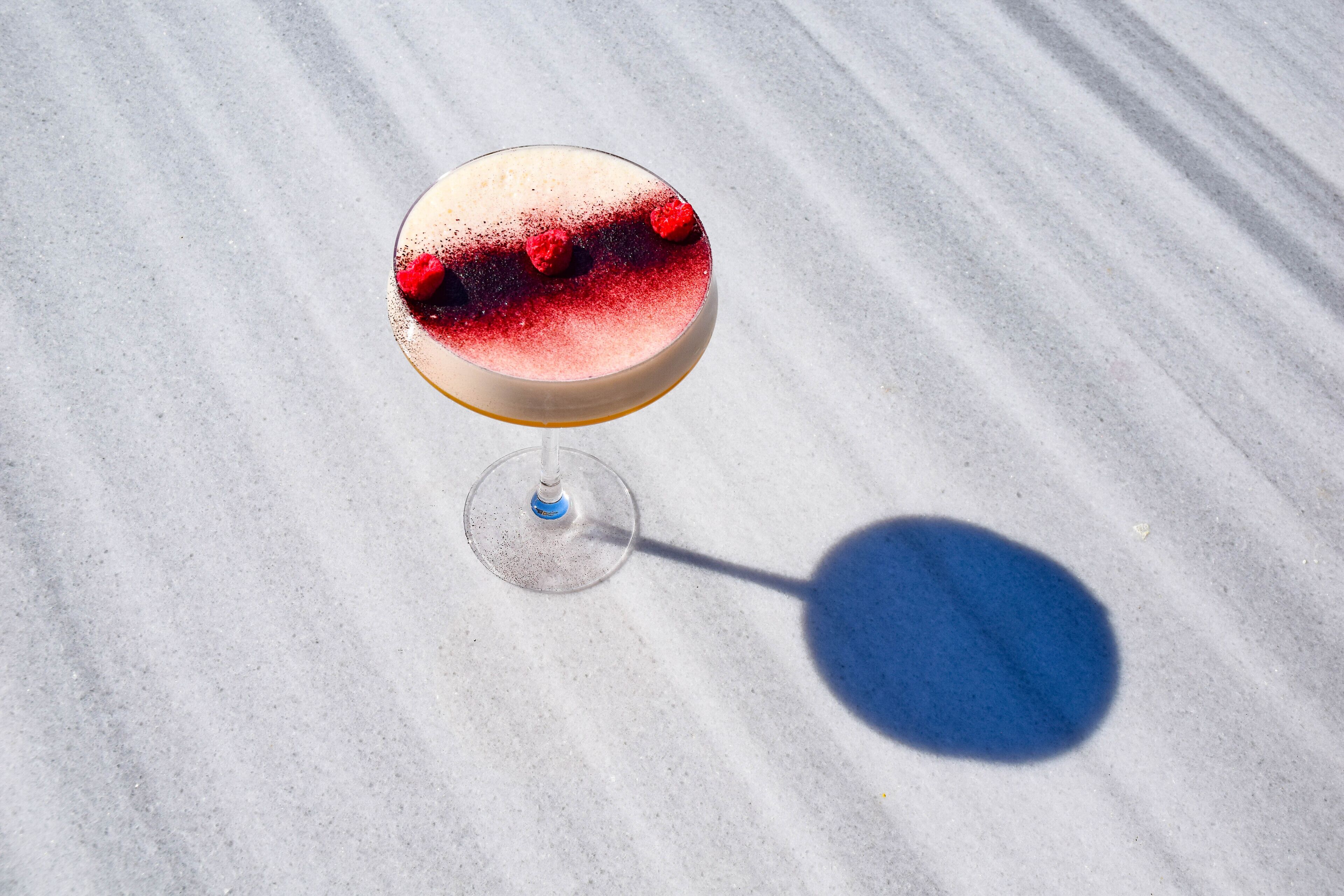 A martini glass with a red rim on a marble surface.