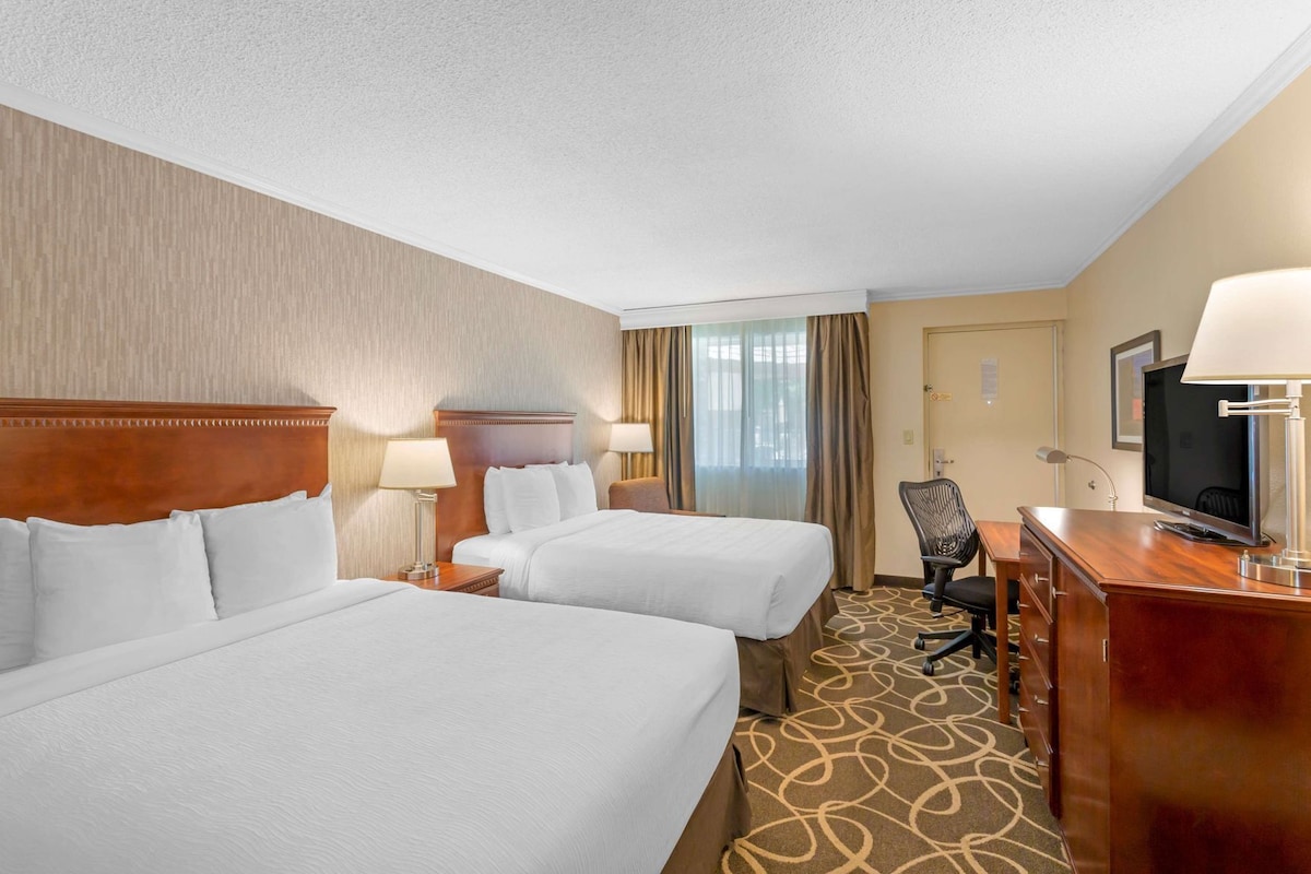 A hotel room with two beds, a desk with a TV, and a chair.