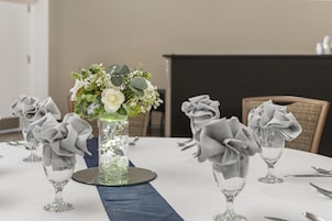 Una mesa dispuesta para un evento formal, con un centro de flores y servilletas dobladas.