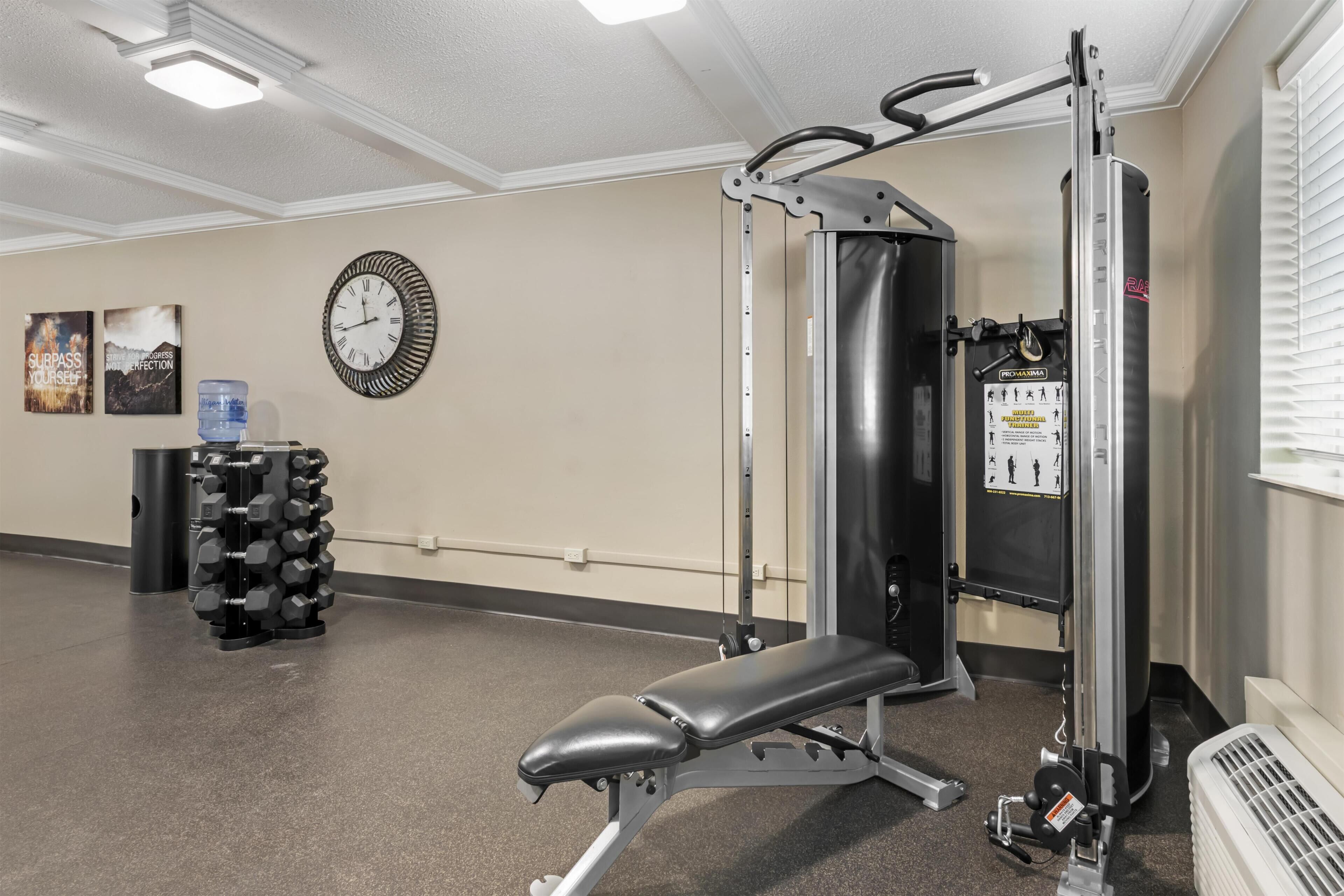 A gym with a bench press, dumbbells, a wall clock, and motivational posters.