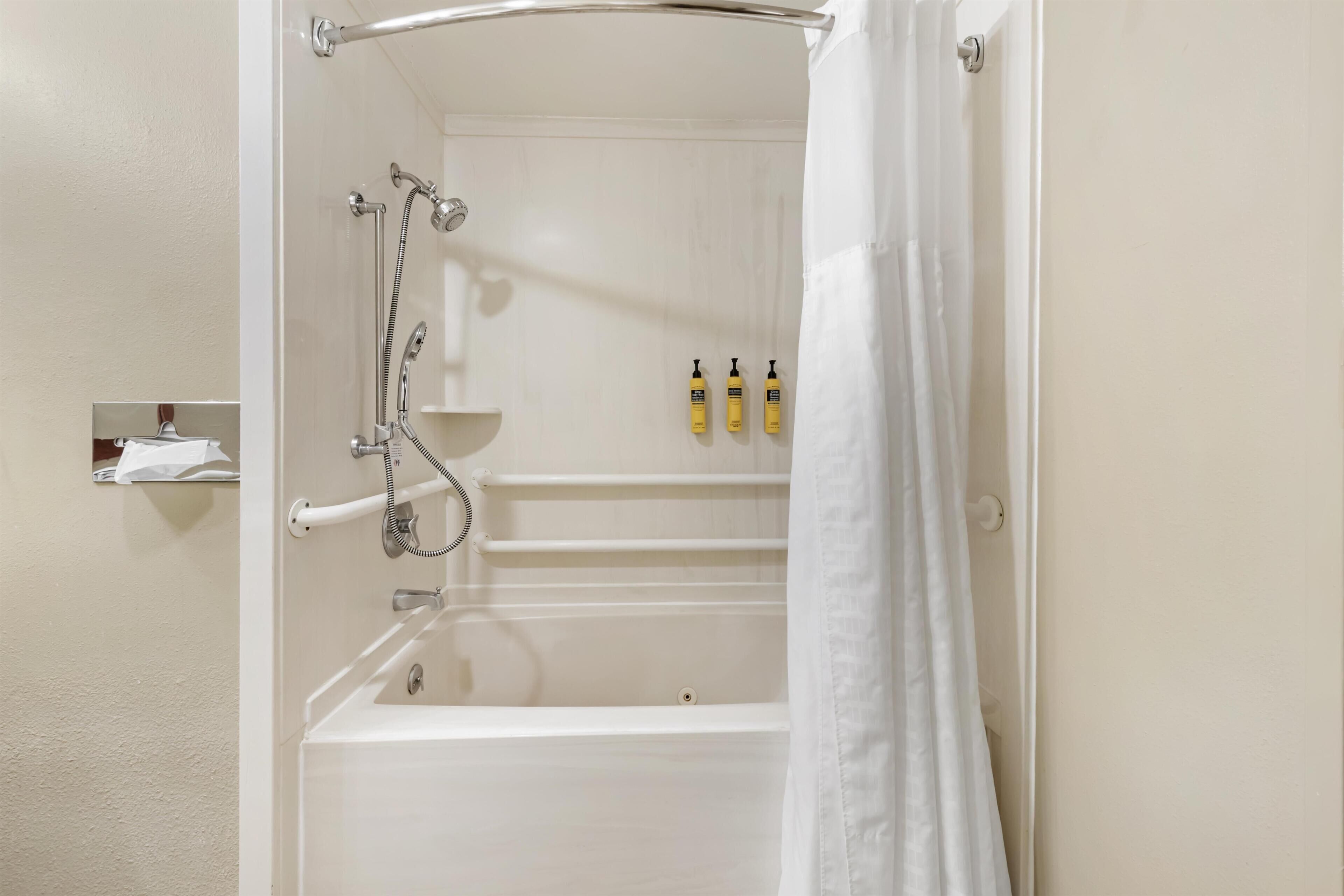 A bathroom with a bathtub, a shower, and a towel rack. There are three bottles of shampoo on the wall.