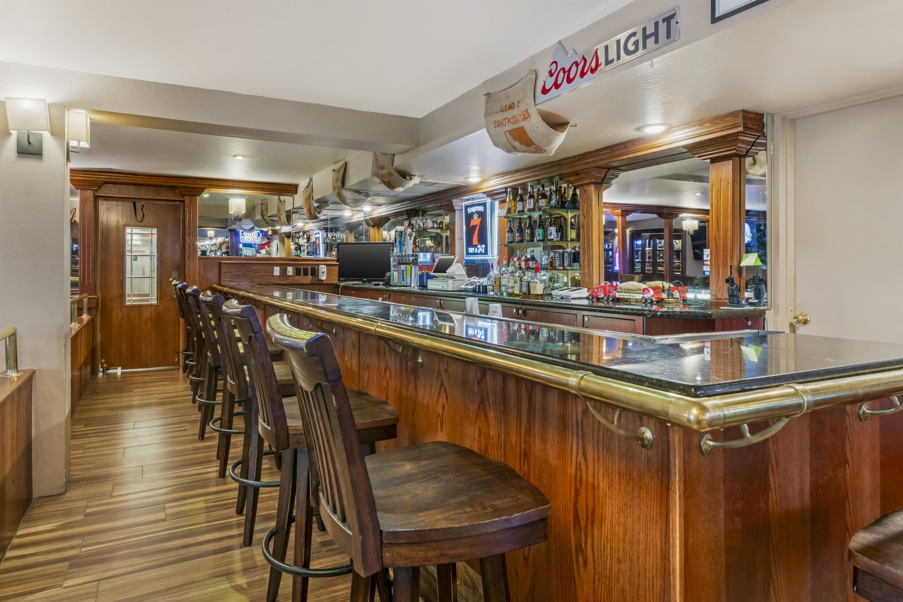 A bar area with a long counter, bar stools, and a Coors Light sign.