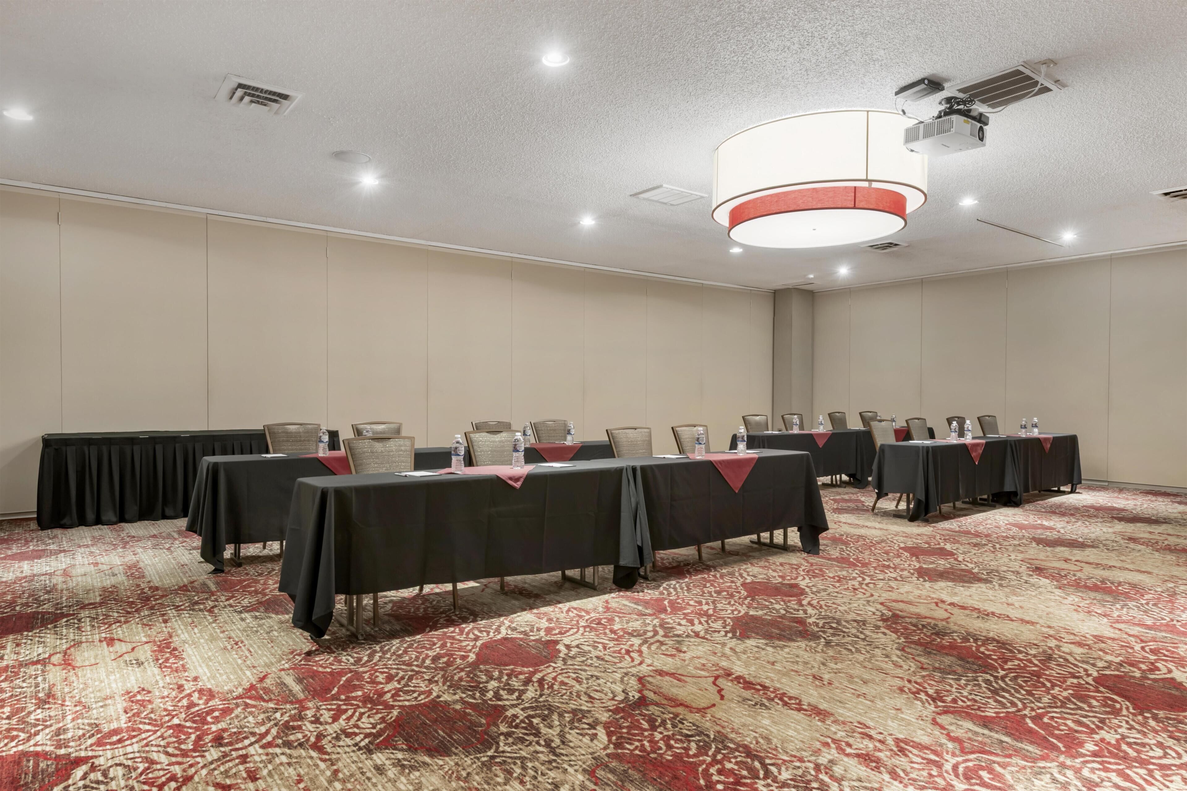 A conference room with multiple tables, chairs, and a carpeted floor.