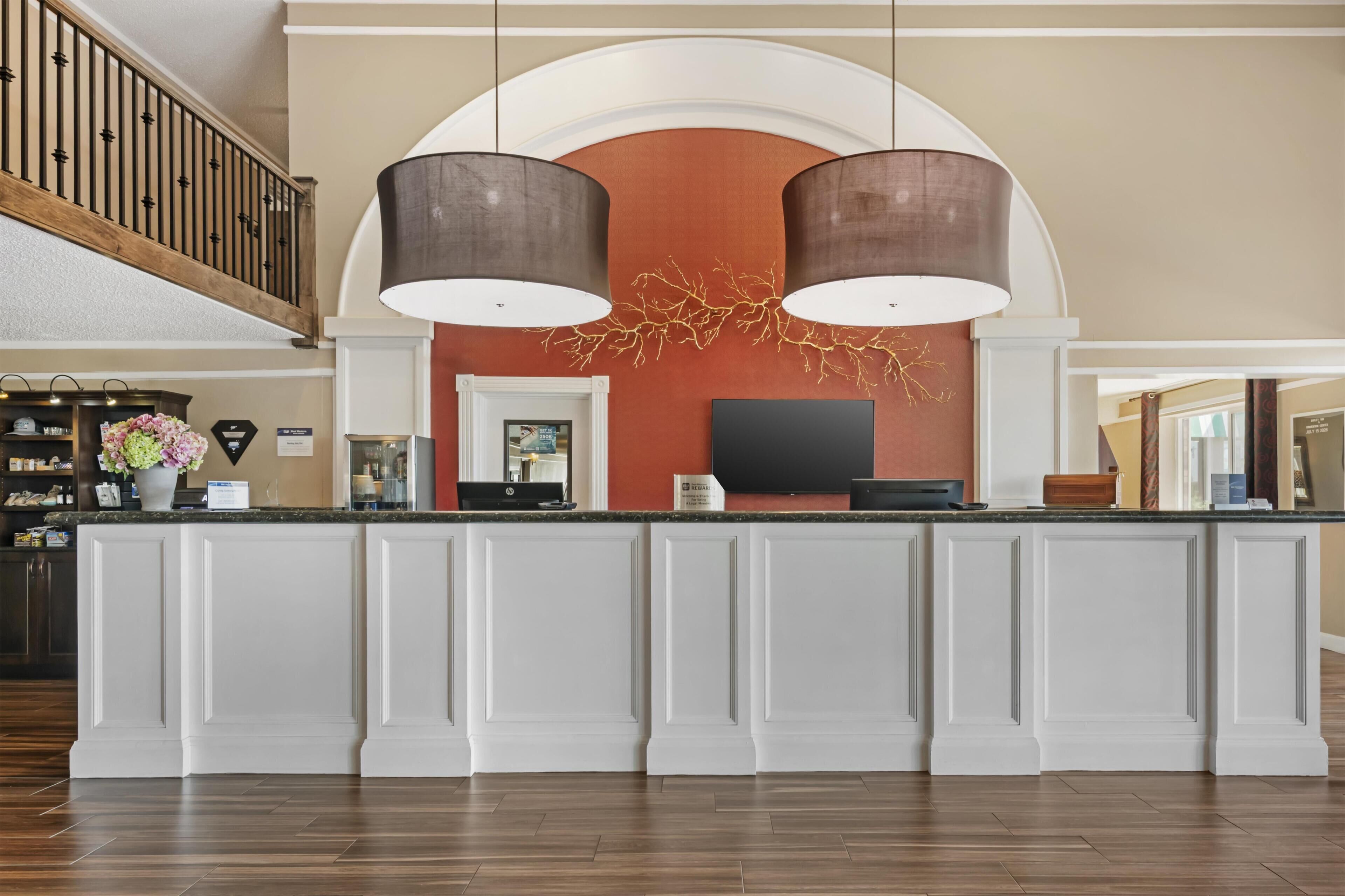 A hotel reception area with a marble counter, two pendant lights, a flat-screen TV, and a decorative wall piece.