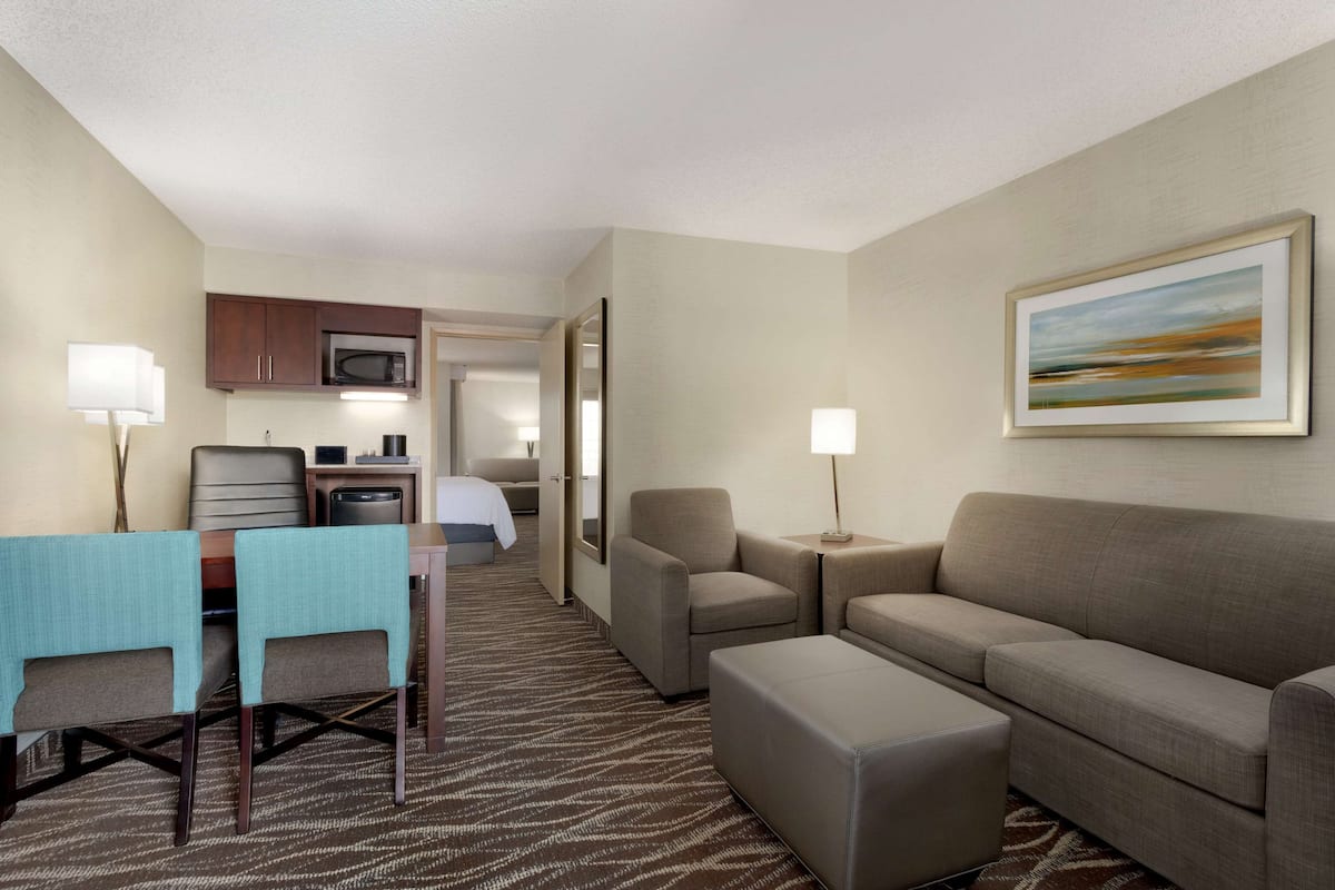 A hotel room with a dining area, a sofa, a coffee table, and a painting on the wall.