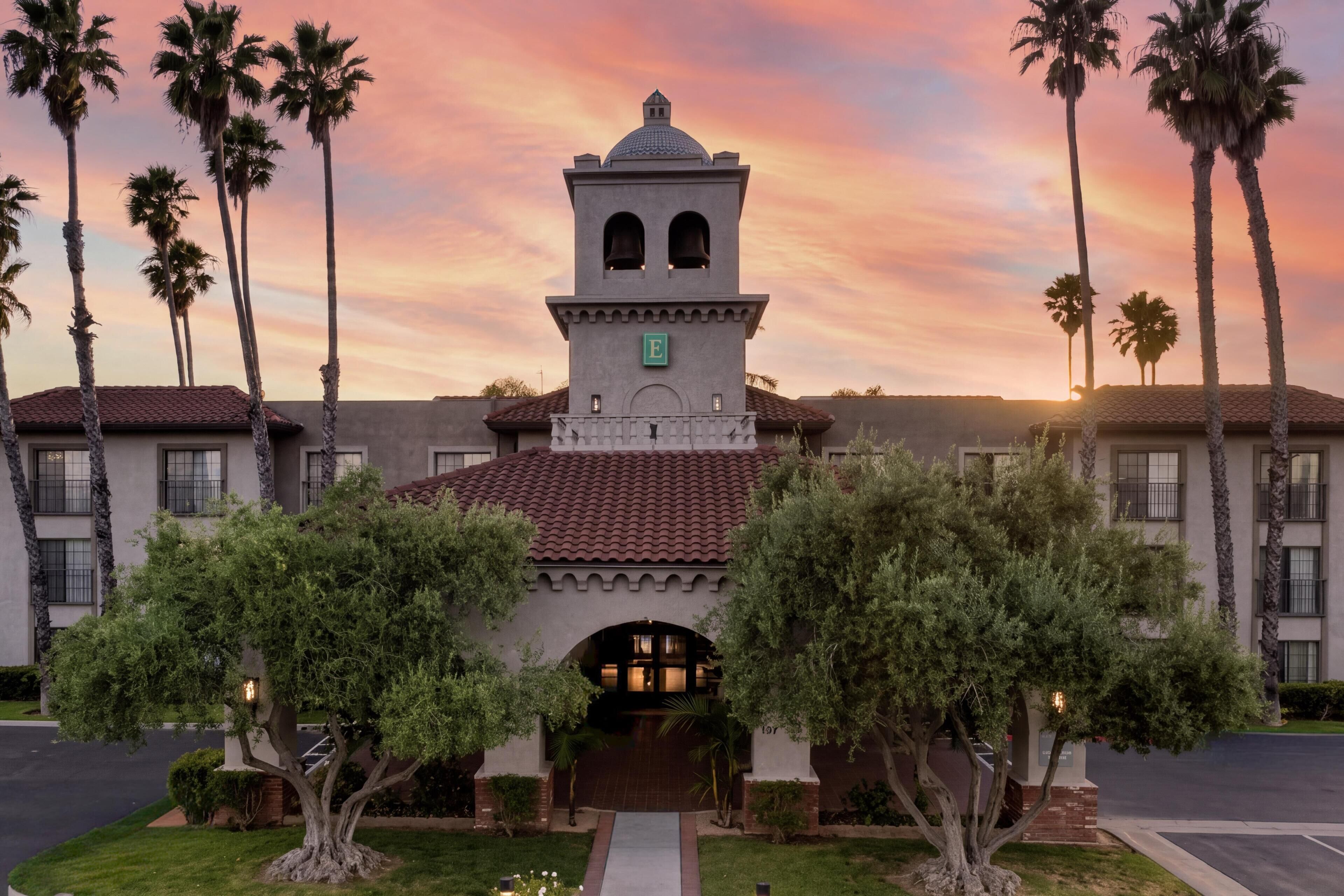 A building with a bell tower, palm trees, and a sunset sky.
