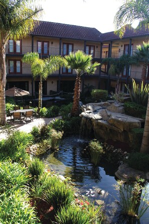 A courtyard with a small pond, palm trees, and a building with balconies. - Embassy Suites by Hilton Lompoc Central Coast (Lompoc)