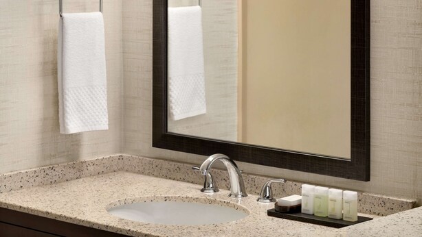 A bathroom with a granite countertop sink, two towel racks, a large mirror, and a soap dispenser shelf. - Embassy Suites by Hilton Lompoc Central Coast (Lompoc)