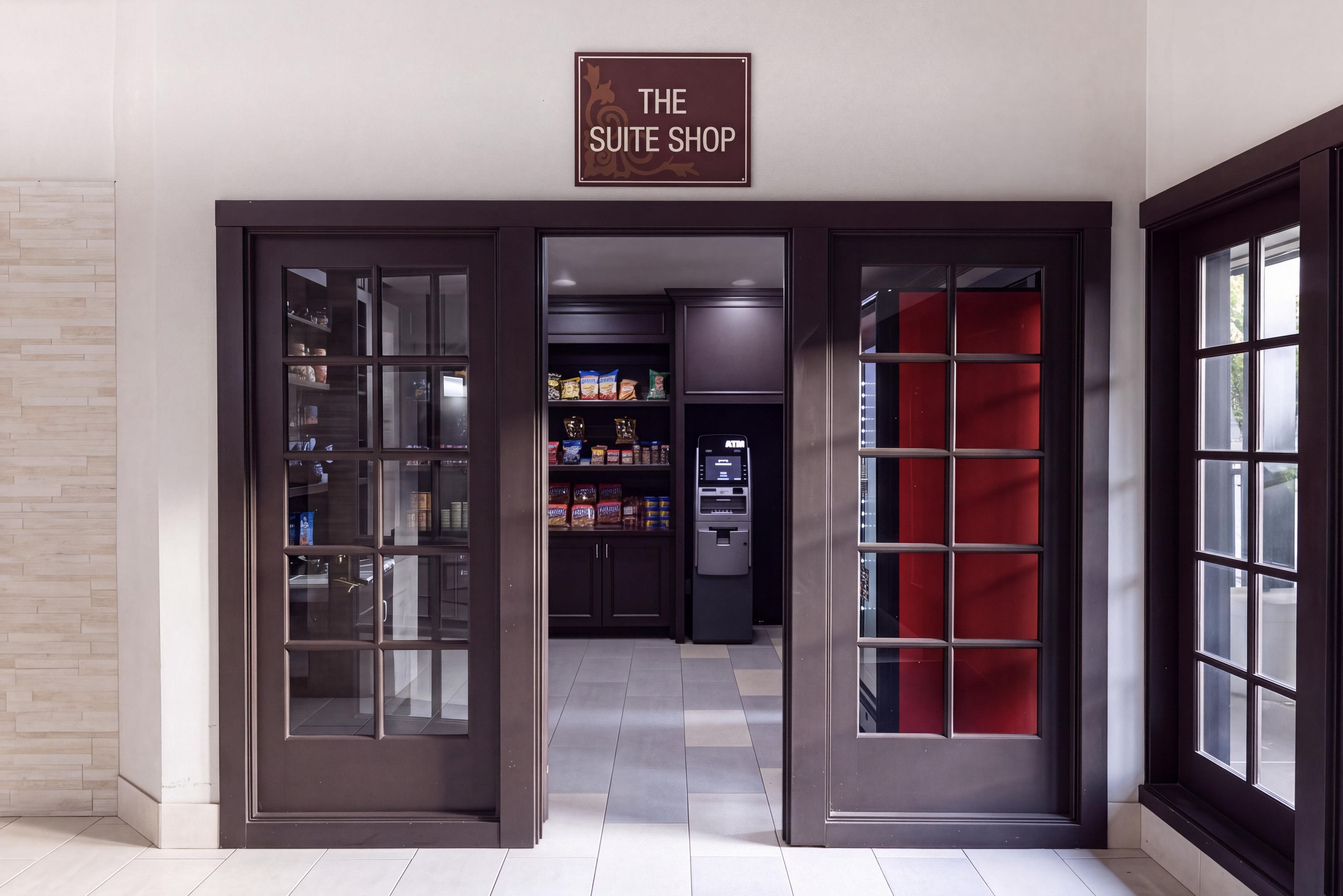 Entrada d'hotel amb un rètol que diu 'The Suite Shop', una porta de vidre, un interior vermell i un caixer automàtic.