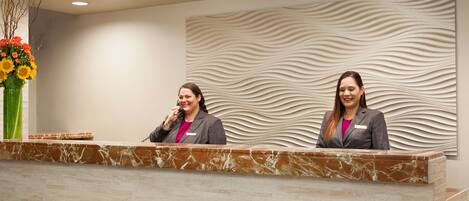 A reception desk with two staff members, a marble counter, and a decorative wall with a wavy pattern.