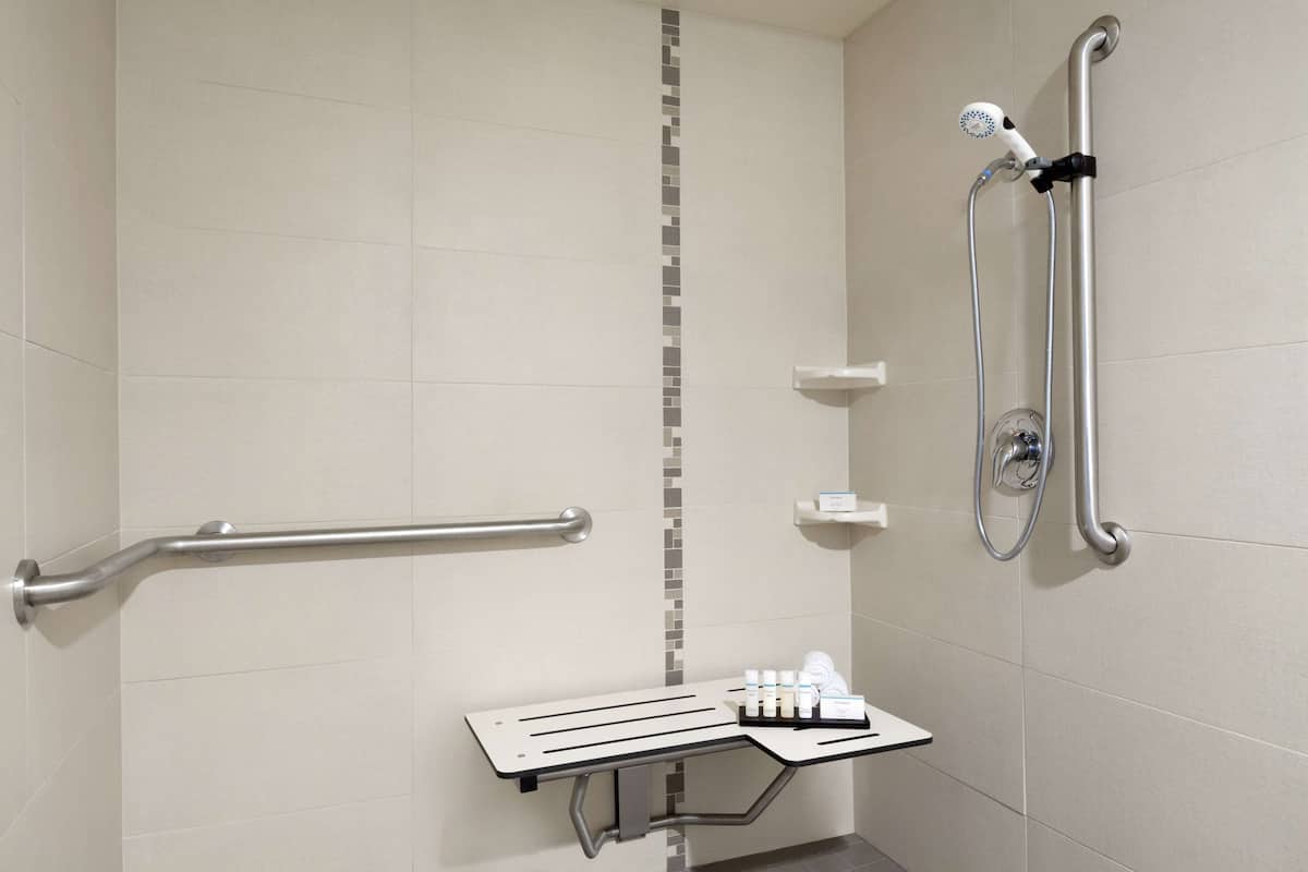 A bathroom with a shower, grab bars, and a small shelf with toiletries.