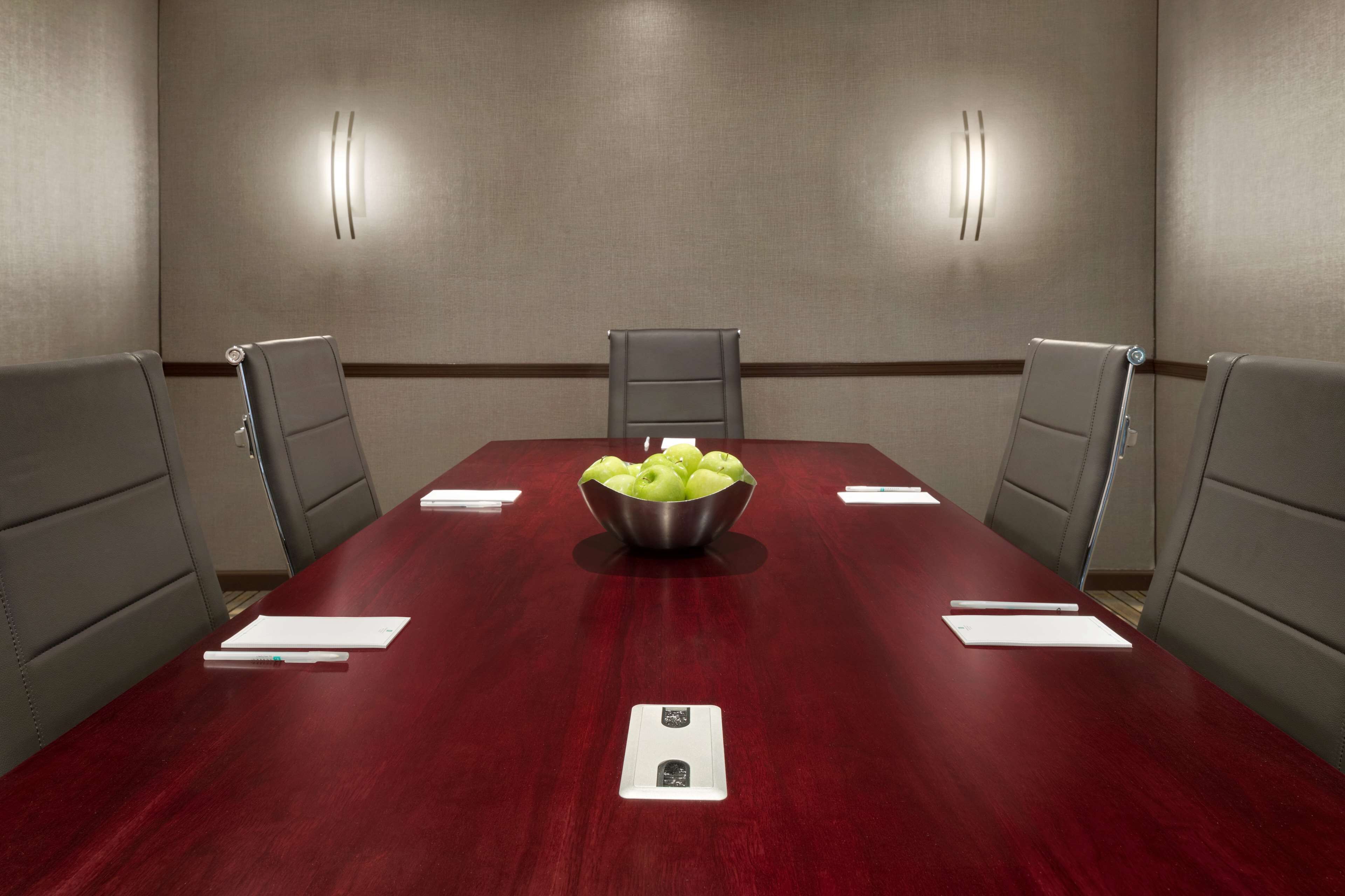 Een vergaderruimte met een rode tafel, vier stoelen, een schaal appels en een wit notitieblok op de tafel.