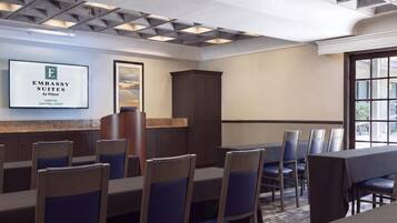 Uma sala de conferências de hotel com uma mesa grande, cadeiras, um armário e uma placa emoldurada na parede.