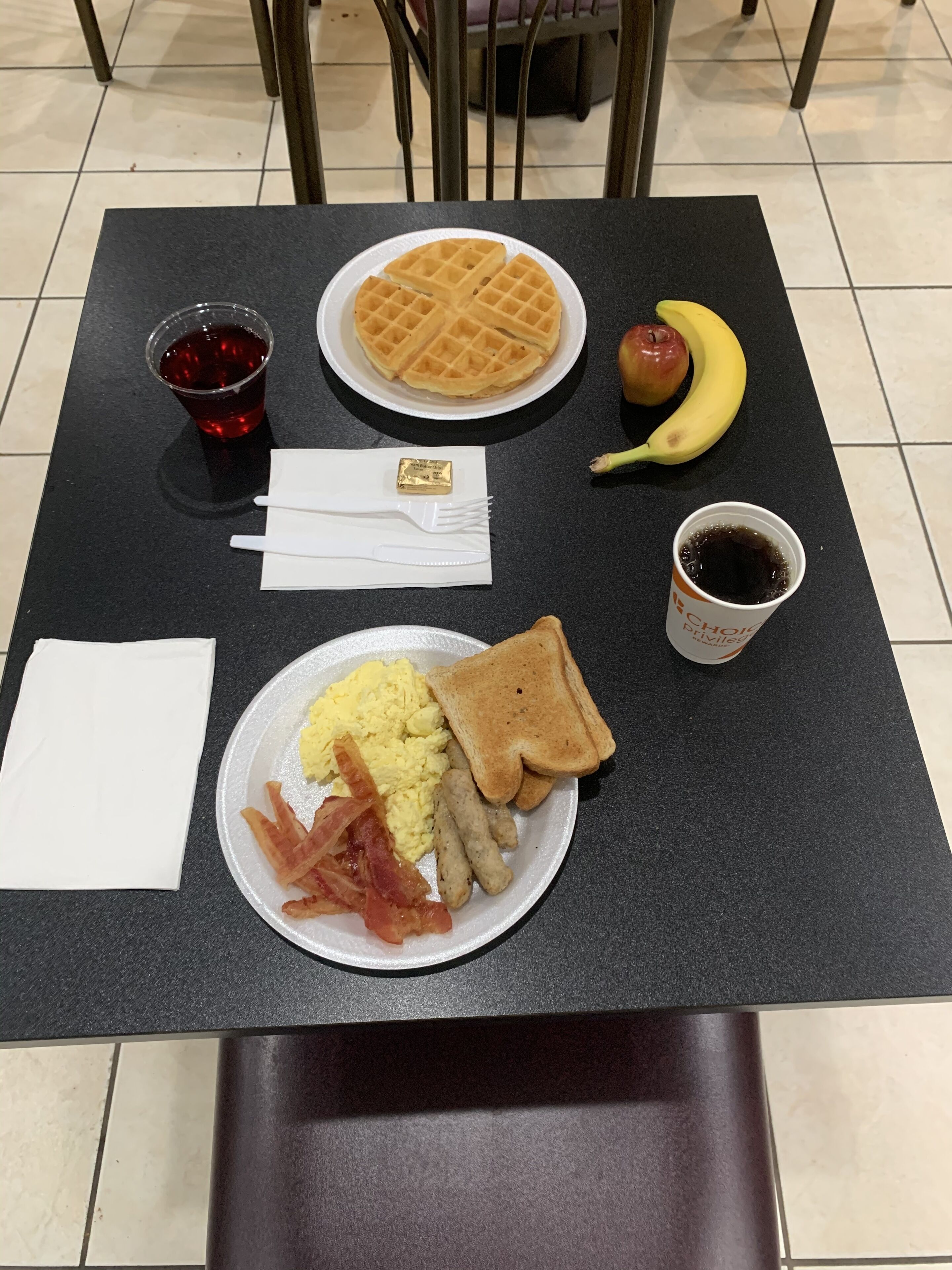 Una mesa con alimentos para el desayuno, incluyendo waffles, tostadas, huevos revueltos, tocino y una taza de café.