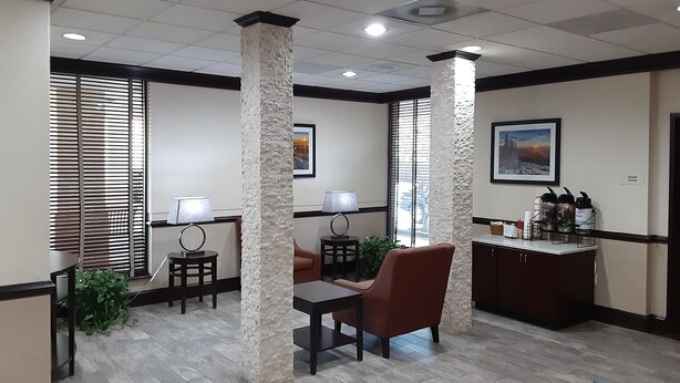 A reception area with a reception desk, two chairs, a small table, a plant, and a wall-mounted lamp. - Quality Inn Morganton Southeast (Morganton)