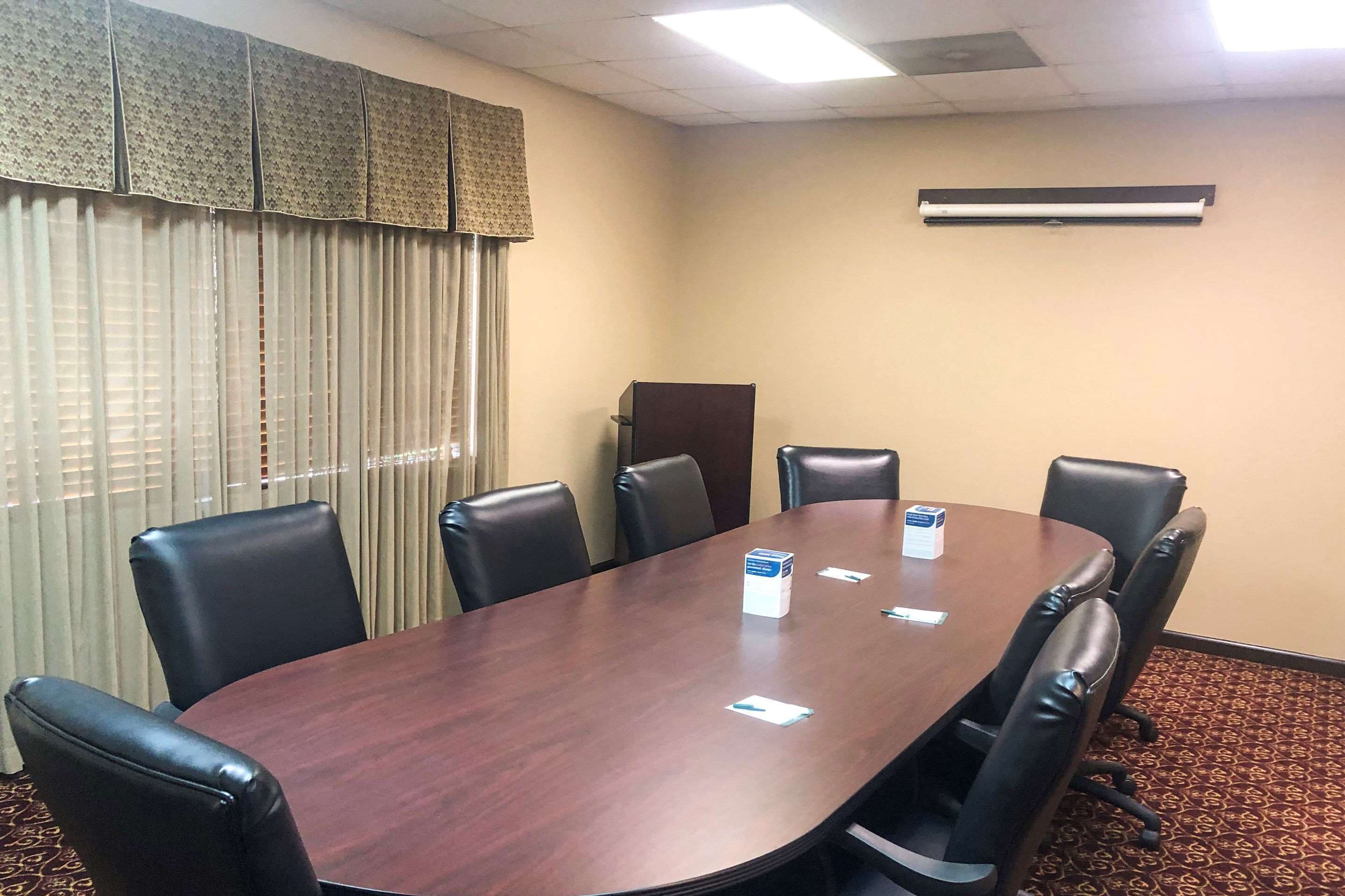 Un salón de conferencias con una mesa grande, seis sillas, una ventana con persianas y un equipo de aire acondicionado en la pared.