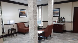 A lobby with two brown leather chairs, a small table, a lamp, a cabinet with bottles, and two large pillars. - Quality Inn Morganton Southeast (Morganton)