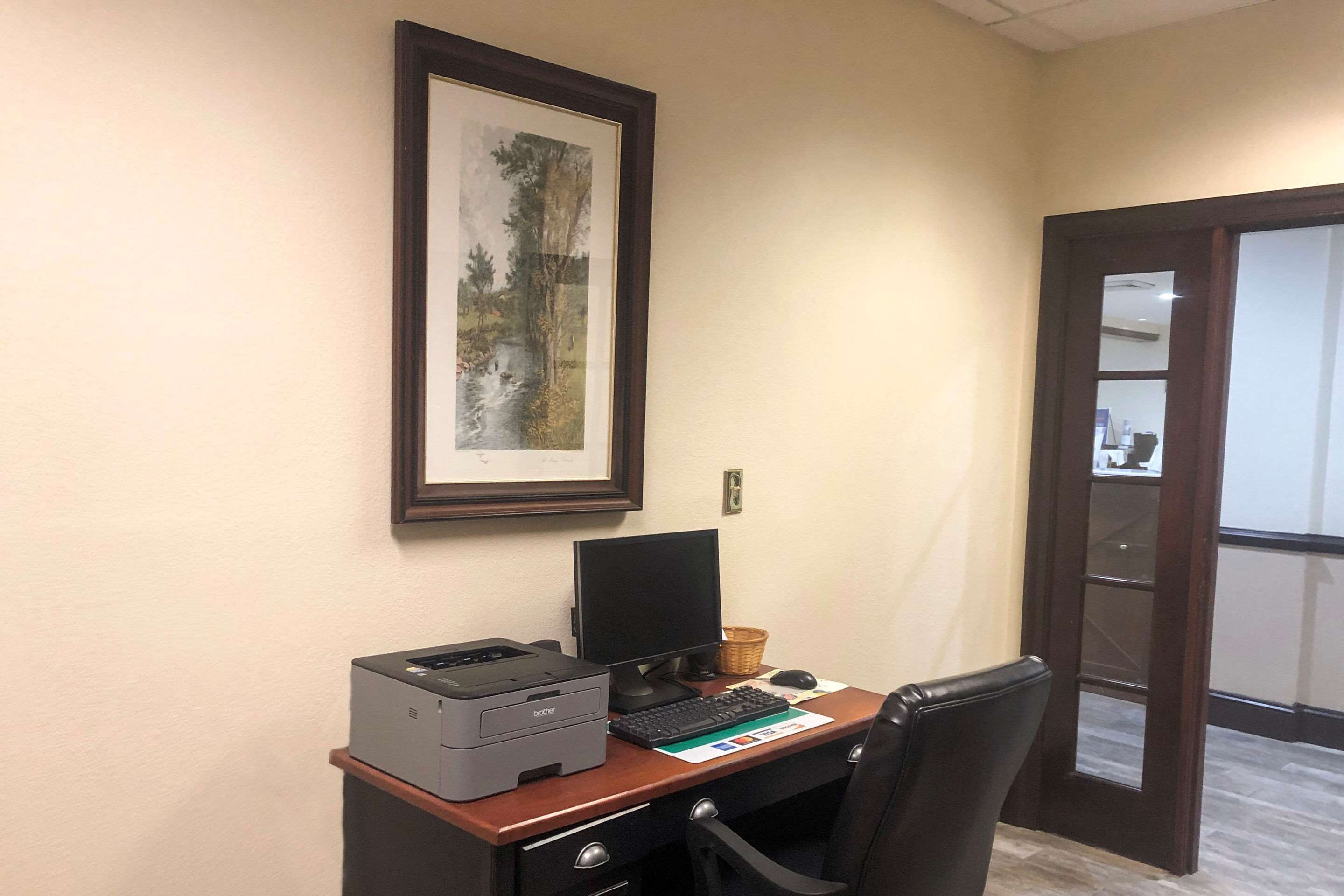A desk with a printer, computer, keyboard, mouse, and a framed picture on the wall.