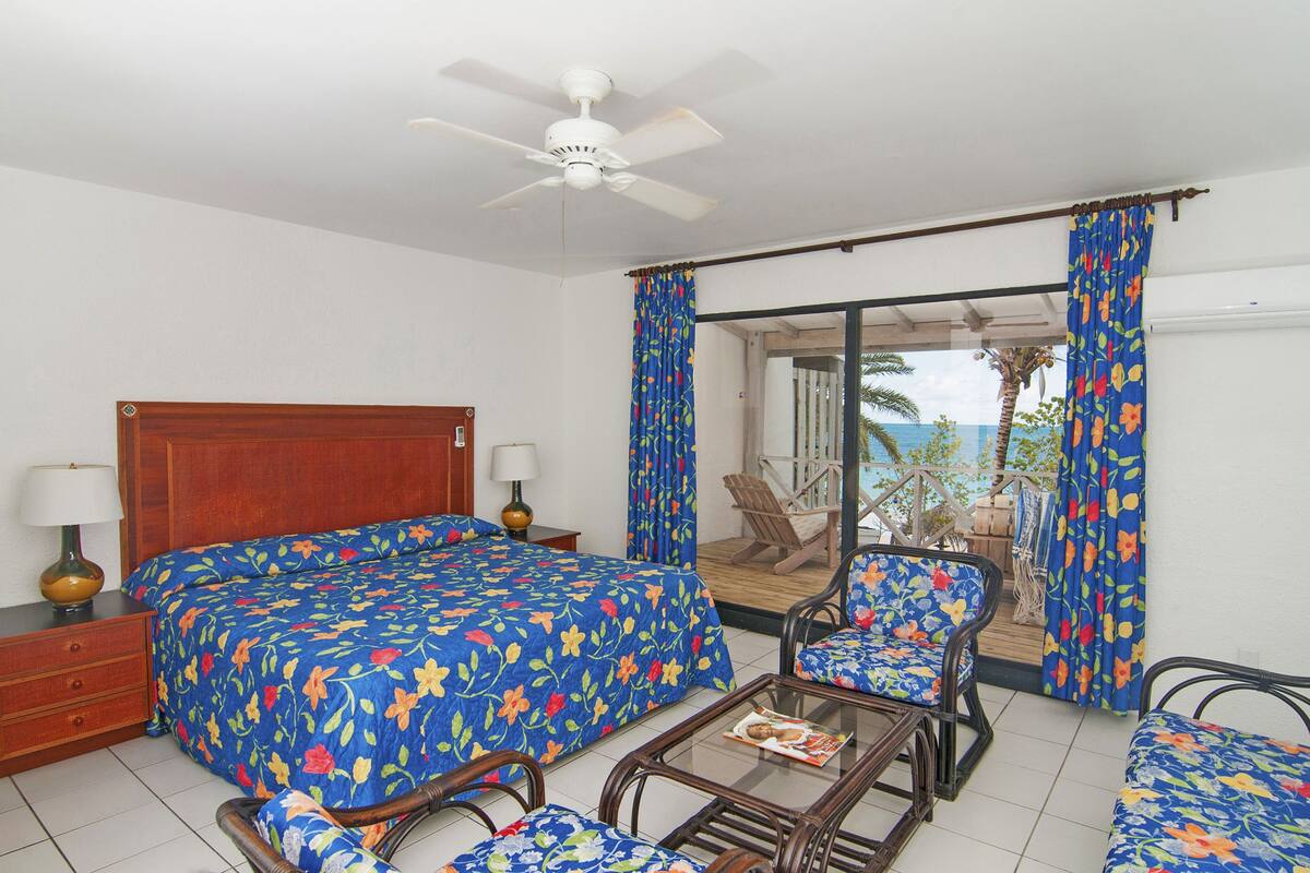 A hotel room with a bed, two chairs, a table, and a balcony with a view.