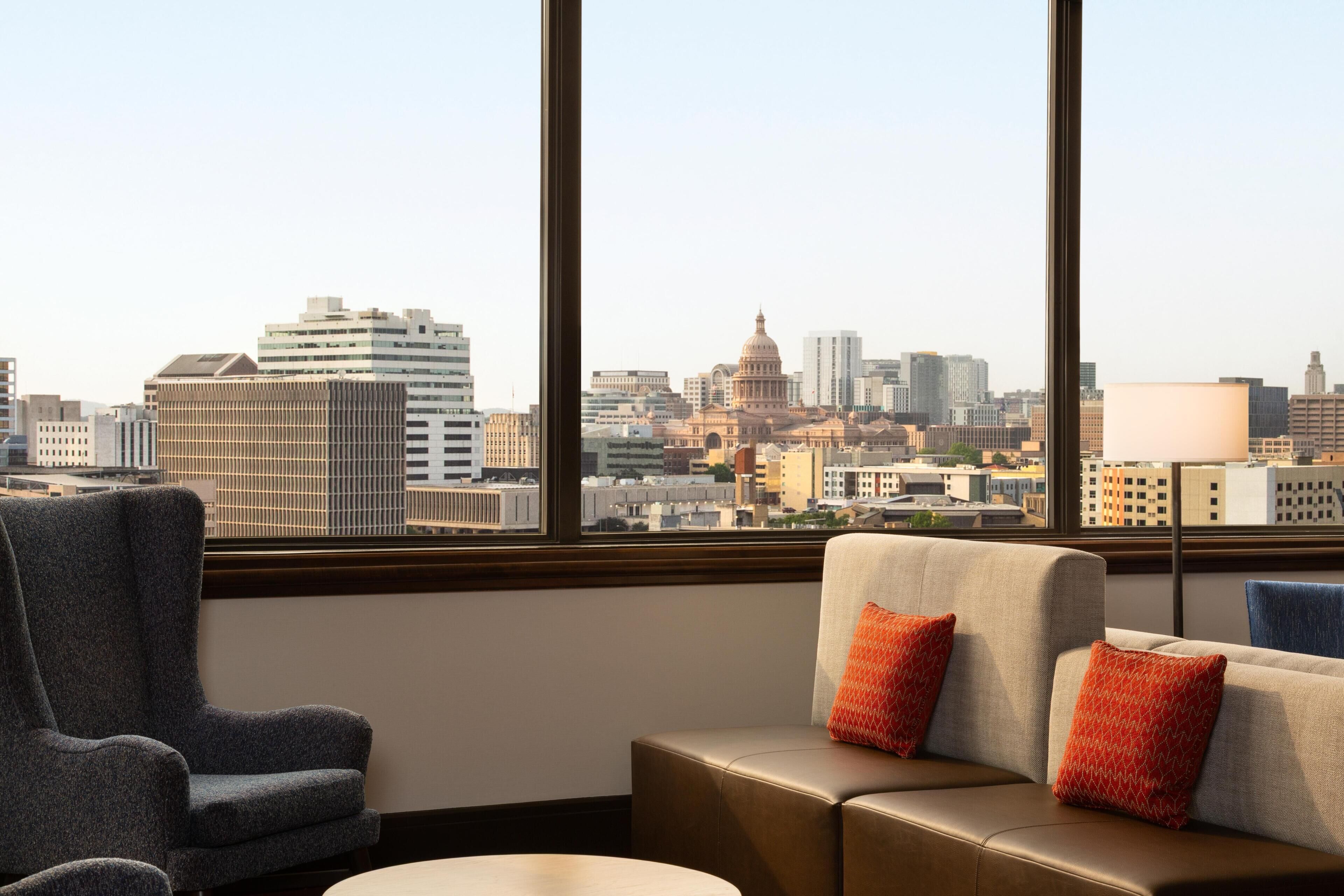 A hotel room with a large window, a sofa, a chair, and a lamp.