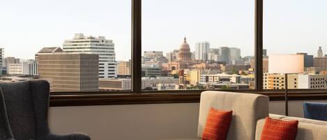 A hotel room with a large window, a sofa, a chair, and a lamp.