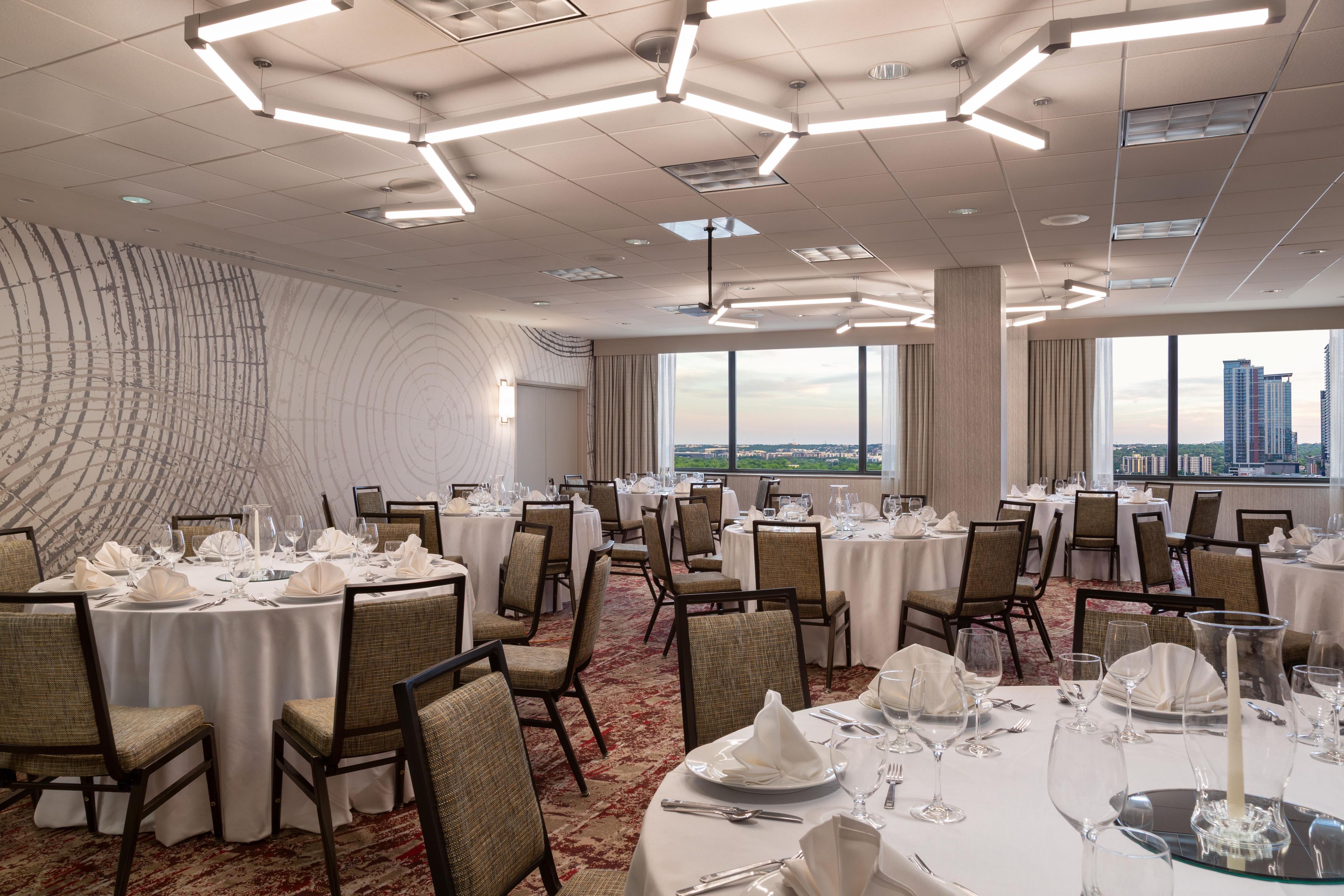 Una sala conferenze con tavoli rotondi, sedie e vista sulla città attraverso ampie finestre.