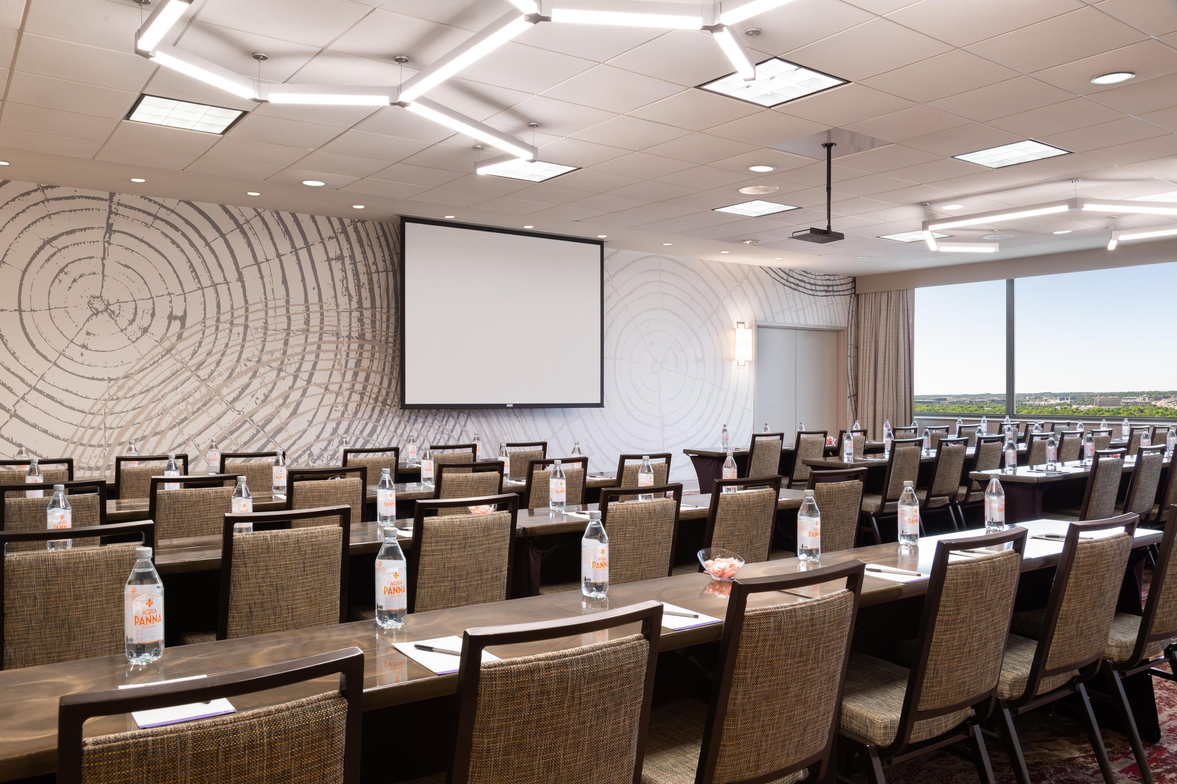 A conference room with tables, chairs, a projector screen, and a large window with a view.
