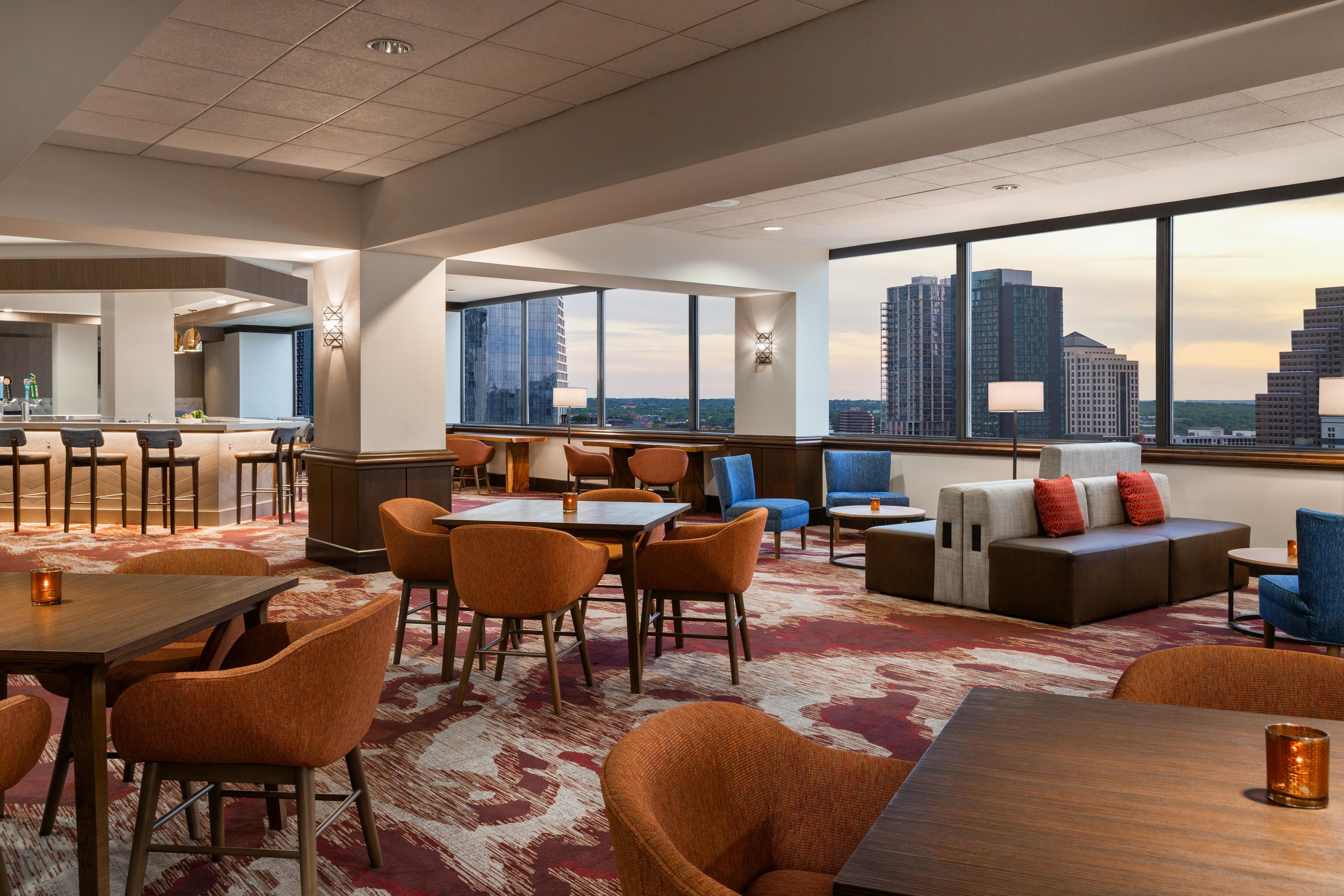 A hotel lobby with a large window offering a city view, a bar area, and seating arrangements.