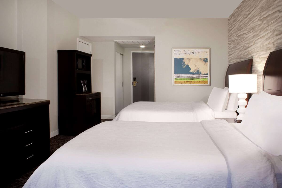 A hotel room with two beds, a television, a wardrobe, and a painting on the wall.