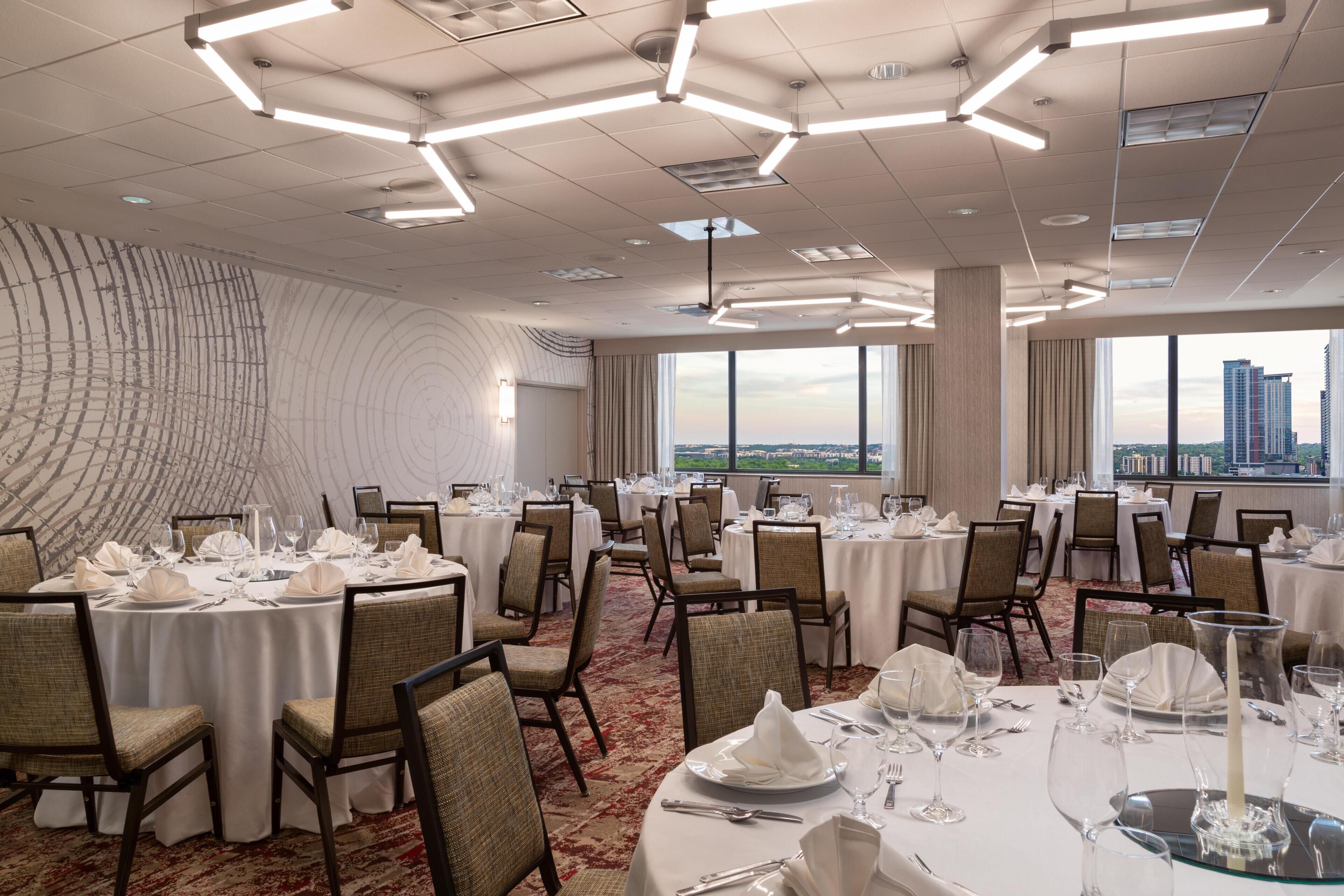 A conference room with round tables, chairs, and a city view through large windows.