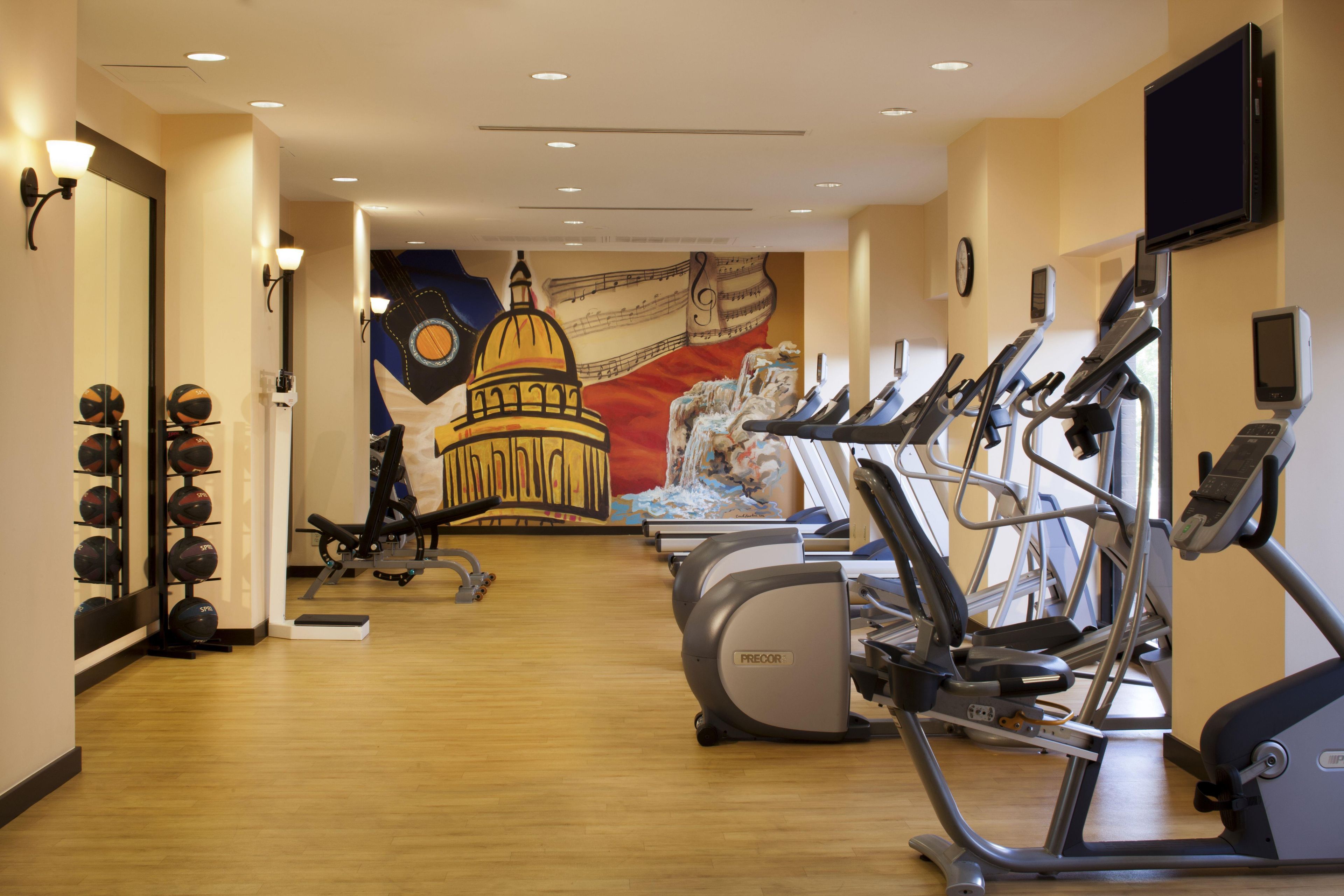 A gym with exercise equipment, a wall mural, and a basketball hoop.