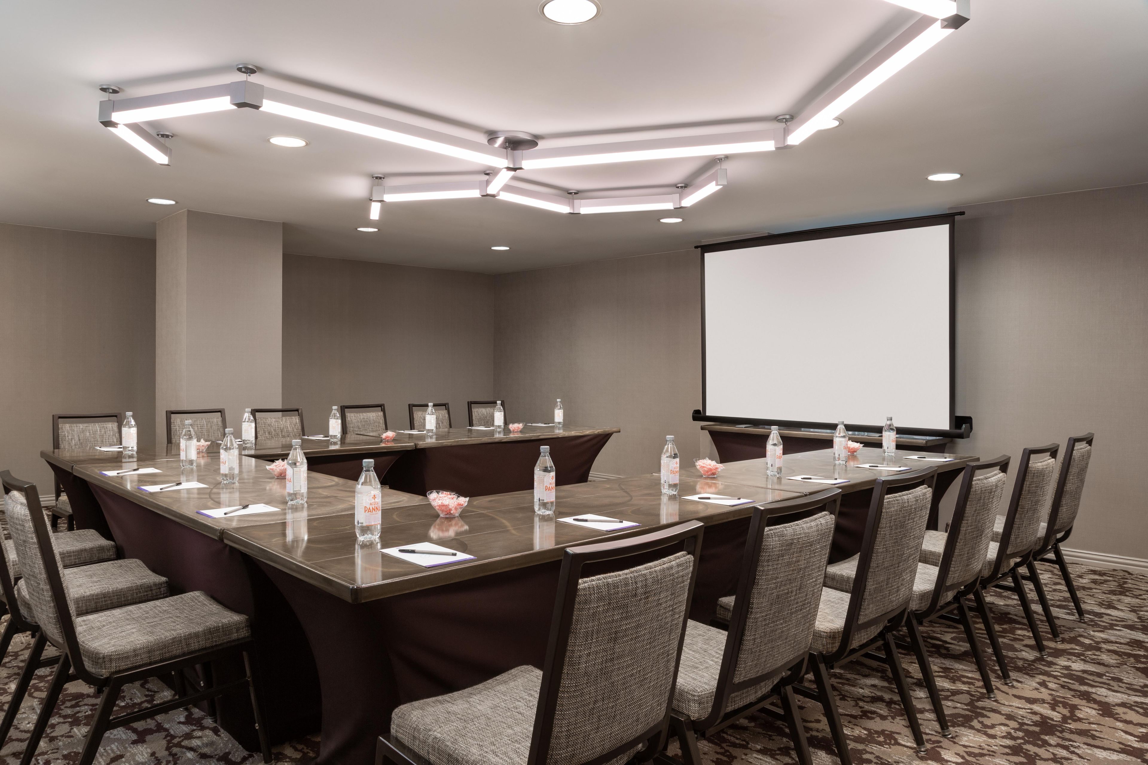 A conference room with a long table, chairs, a projector screen, and a carpeted floor.
