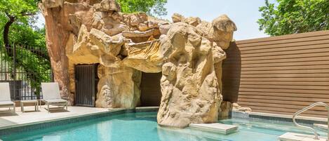 Ein Pool mit einer natürlichen Felsformation, Liegestühlen und einem Holzzaun.