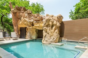 Une piscine bordée de rochers naturels, avec des chaises longues et une clôture en bois.