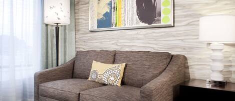 A modern living room with a grey sofa, a decorative pillow, a framed abstract artwork, a floor lamp, and a dark wooden side table.