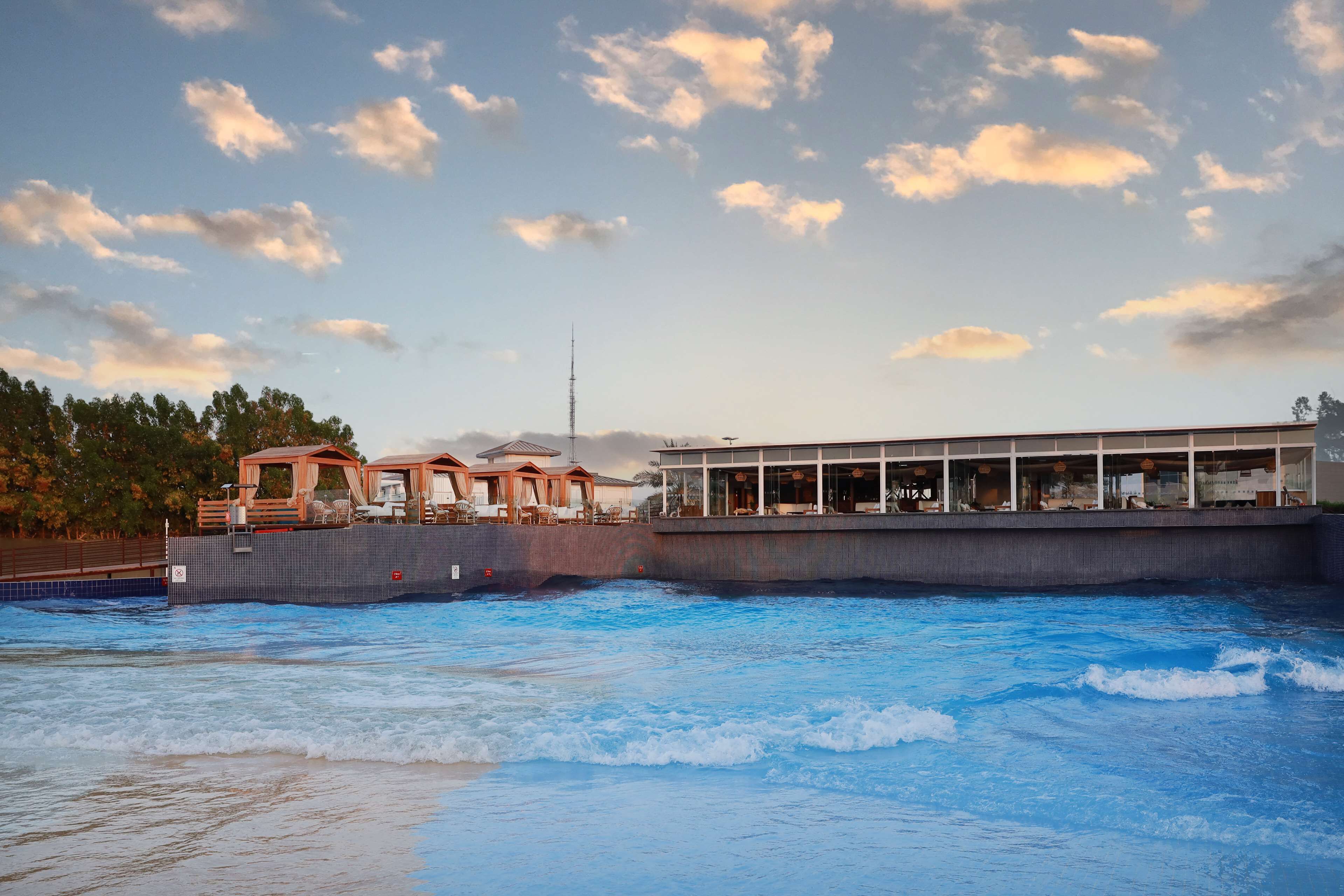 Un hotel frente al agua con piscina, una terraza de madera y un edificio con grandes ventanales.