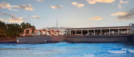 Un hotel frente al agua con piscina, una terraza de madera y un edificio con grandes ventanales.