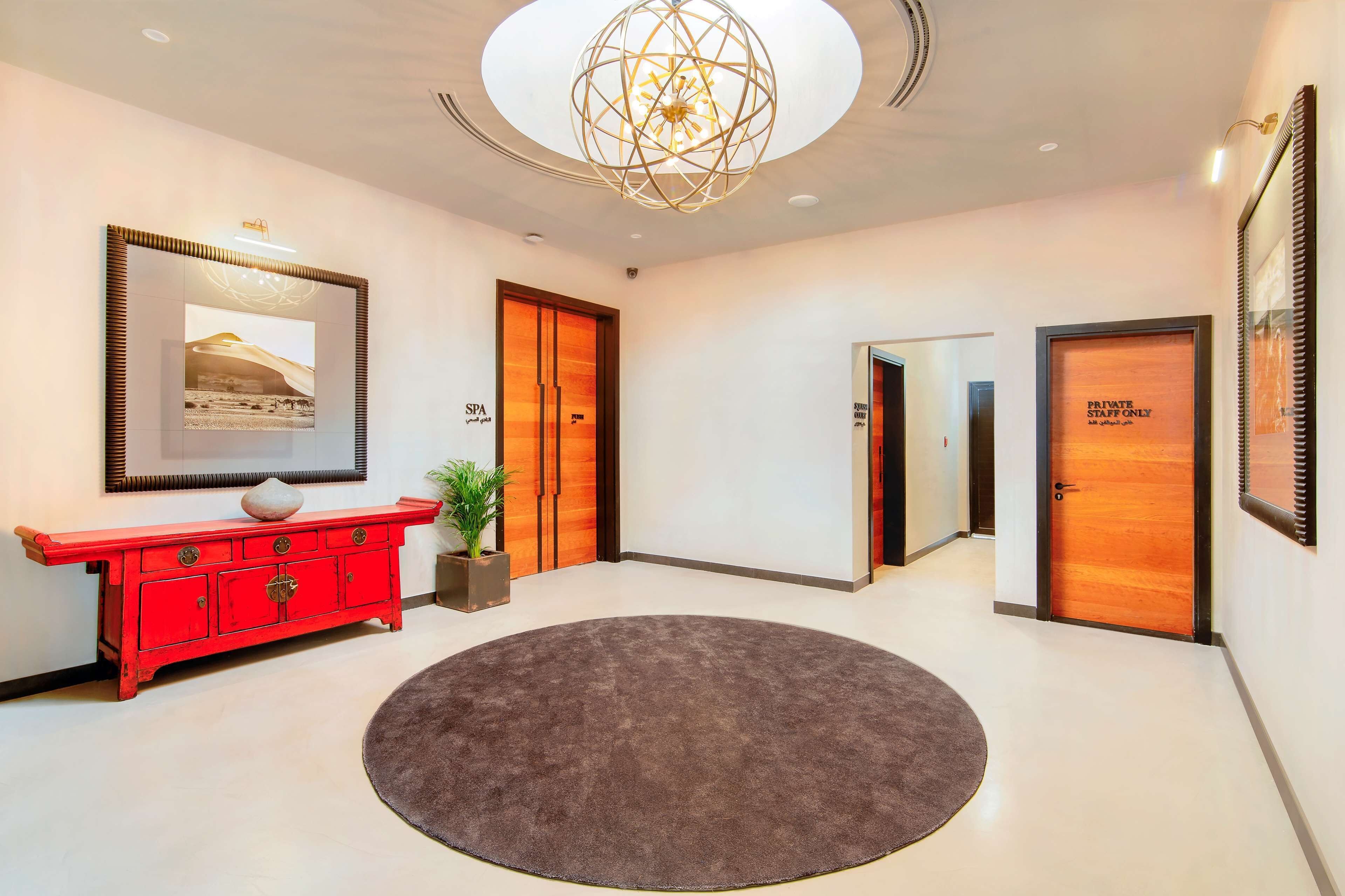 A modern lobby with a red console, a round rug, a ceiling light, and two doors labeled "SPA" and "PRIVATE STAFF ONLY".