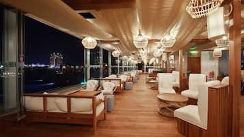 A deck with wooden flooring, white upholstered chairs, and hanging wicker lamps.