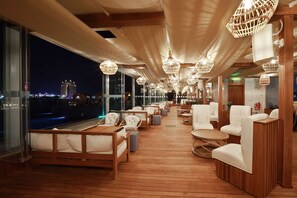 Une terrasse avec un plancher en bois, des chaises blanches recouvertes de tissu et des lampes en osier suspendues.