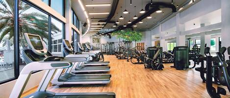 A gym with treadmills, weight machines, and a large window with a view of palm trees.