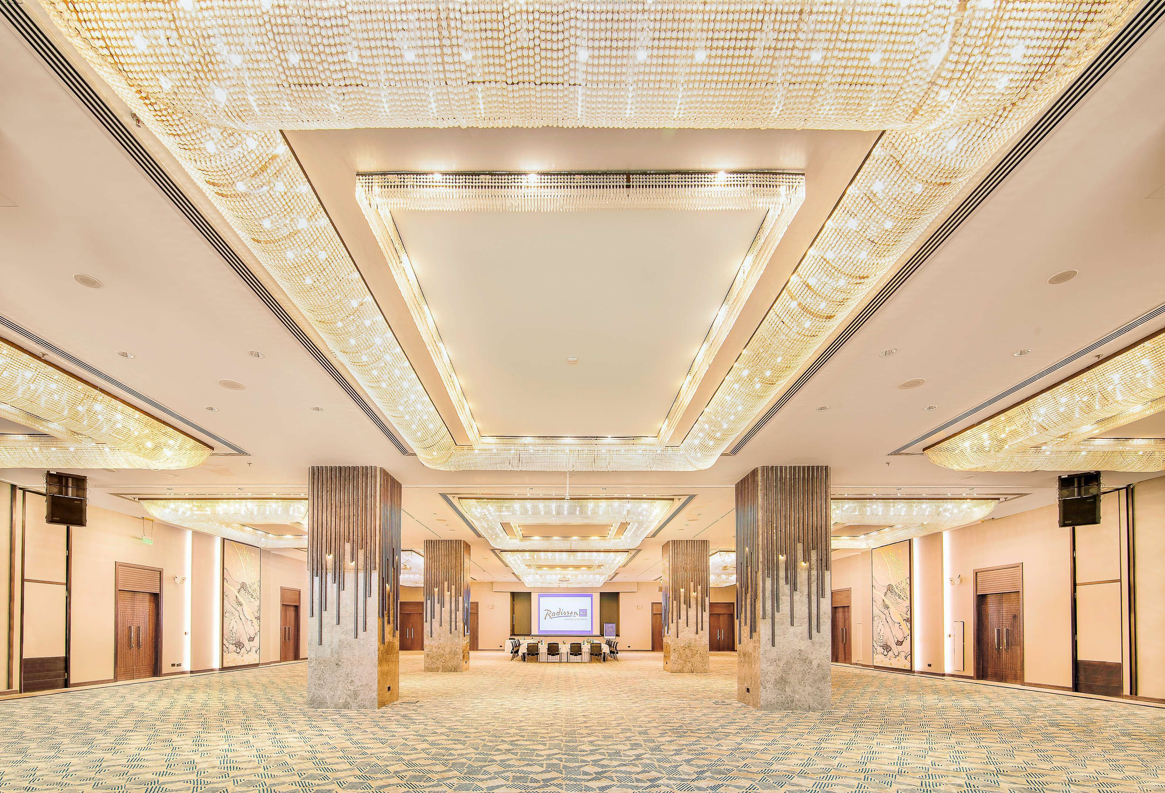A spacious conference room with a large screen, high ceilings with intricate lighting, and a patterned floor.